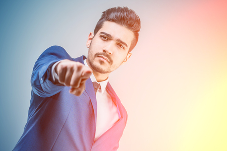 Young attractive man in a blue suit showing a finger forward in bright lightの写真素材