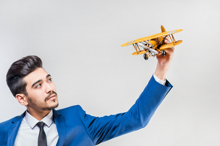Young attractive man in a blue suit holding a yellow airplane model on a gray background. Isolatedの写真素材
