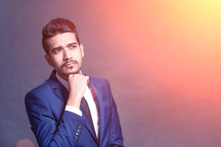 Pensive young attractive man in a blue suit in the sunlightの写真素材