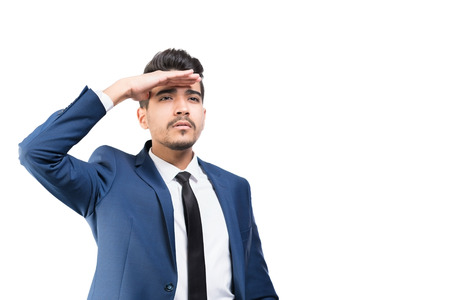 Young attractive man in a blue suit looks away holding his hand over his eyes on a white background....