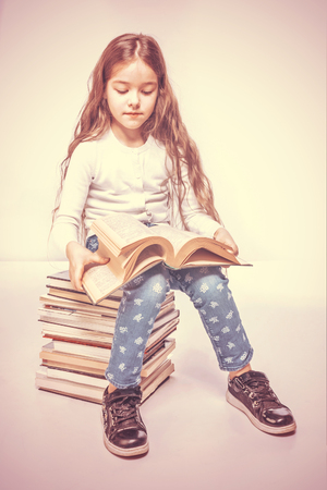 Cute girl with a book sitting on a pile of books on a white background. Tonedの写真素材