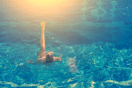 Woman in bikini swims in the pool in the sunlightの写真素材
