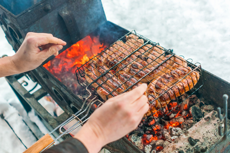 Man warms his hands over the brazier with sausages grilled in winterの写真素材