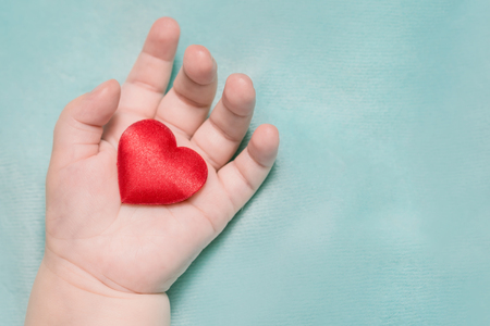 Red heart in the hand of a baby on a blue backgroundの写真素材