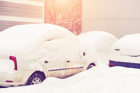 Parked car covered with snow in the sunlightの写真素材