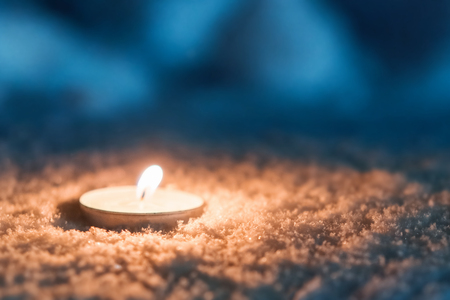 Burning candle in the snow at dark