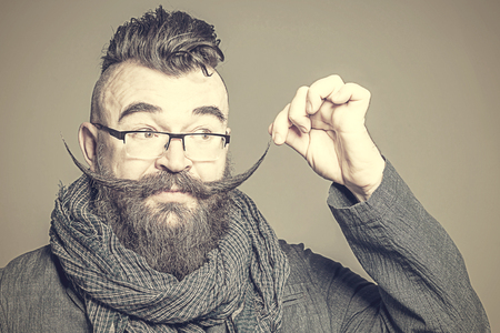 Adult bearded man with a mohawk hairstyle touches long mustache. Tonedの写真素材