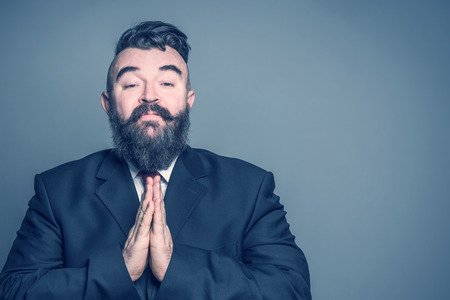 Imploring adult bearded man in a suit  on a gray backgroundの写真素材