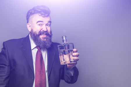 Adult bearded man in suit holding a bottle of alcohol on a purple backgroundの写真素材