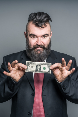 Adult bearded man in a suit holding a dollar on a gray backgroundの写真素材