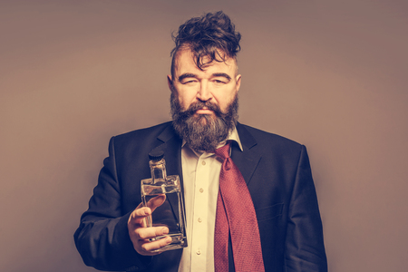 Disheveled drunk man in a suit with a bottle of alcohol in his hand on a brown backgroundの写真素材