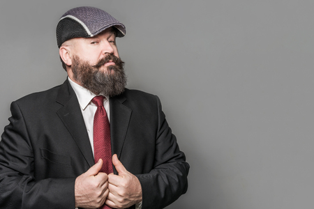 Adult bearded man in a suit and cap on a gray backgroundの写真素材