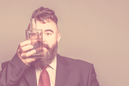 Adult bearded man in suit looking through a bottle of alcohol. Tonedの写真素材