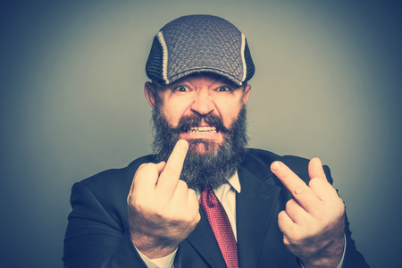 Angry adult bearded man in a suit and cap showing middle fingers. Tonedの写真素材