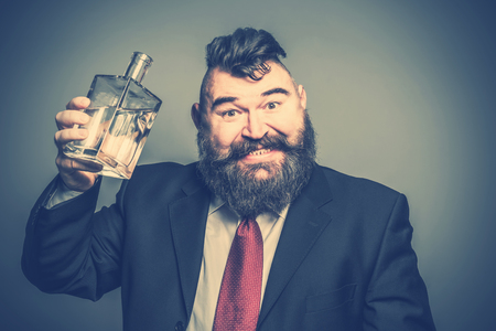 Crazy bearded man in suit picks up a bottle of alcohol. Tonedの写真素材