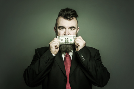 Adult bearded man in a suit closes mouth with Dollar on green backgroundの写真素材