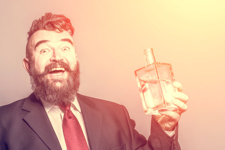 Happy adult bearded man in suit  holding a bottle of alcohol in the sunlightの写真素材