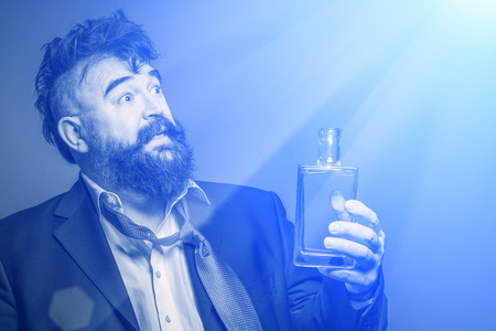 Drunken bearded man in suit with a bottle of alcohol in his hand looking at the blue rays of lightの写真素材