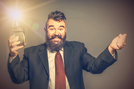Happy adult bearded man in suit pulled the cork out of the luminous bottle with alcoholの写真素材