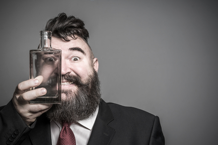 Smiling adult bearded man in suit looking through a glass bottle of alcohol. Tonedの写真素材