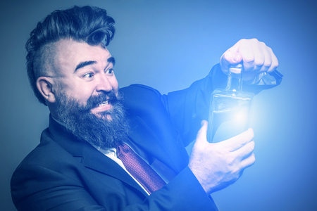Adult bearded man in suit pulling out the cork from a luminous bottle with alcoholの写真素材