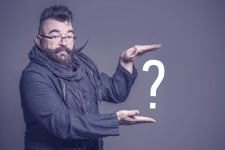 Adult bearded man with a very long mustache holding question mark in hands on a purple background. Tonedの写真素材