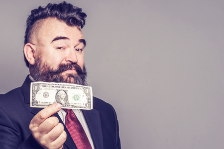 Adult bearded man in a suit holding a dollar on gray backgroundの写真素材