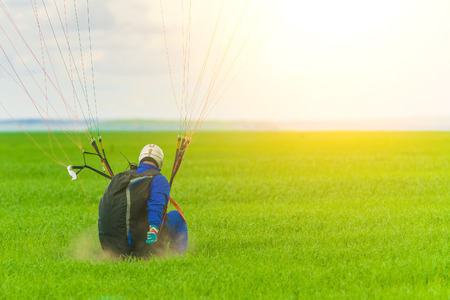 Man on a paraglider during a landing on a green field in the sunlightの写真素材