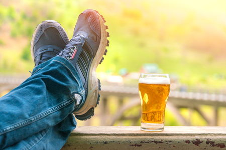Legs in jeans and sneakers next to a mug of beerの写真素材