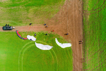 View from the drone of the people are preparing to fly on paragliders on the green field