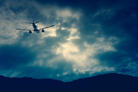 An airplane flying through a dramatic raincloud sky over a mountain range in the horizon.の写真素材