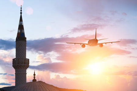 A plane flying in the evening sky above the minaretの写真素材