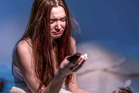 heartbroken. Get the bad news. Get upset. depression. broken heart. A woman with a face dirty from mascara sits in bed and cries, holding a phone in her hands. to suffer.の写真素材