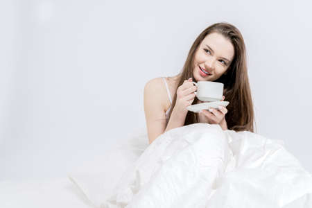 White bedroom. good morning. The brunette is holding a cup with a hot drink. A woman is sitting in...