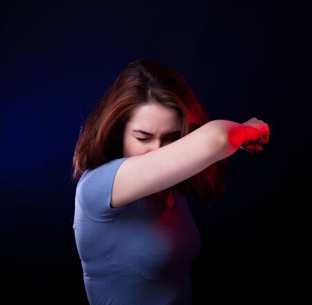 young woman sneeze in her arm. studio shot. portraitの写真素材