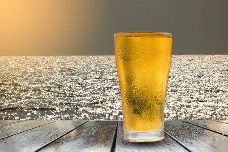 Beer golden white bubbles in the glass on wooden table with beautiful golden sunlight and sea background.の写真素材