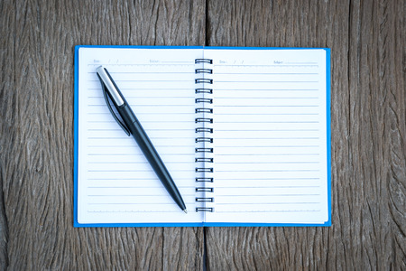 Place the pen on a blank page of a notebook on old wooden background.の写真素材