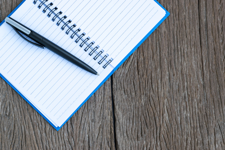 Place the pen on a blank page of a notebook on old wooden background.の写真素材