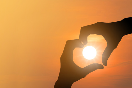 Silhouette of hand made heart symbol across the sun was falling.の写真素材
