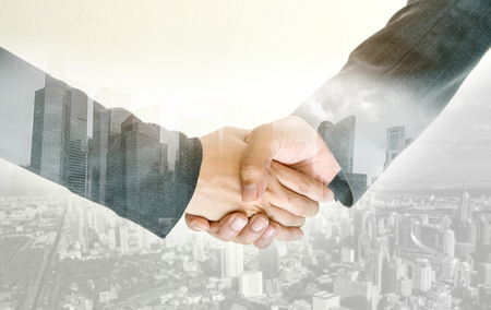 Closeup of double exposure handshake of business peoples on the city background.の写真素材