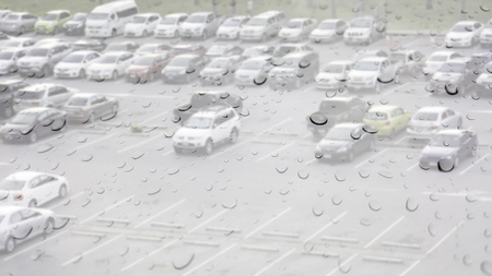 Double exposure of raindrops perched on the glass while it is raining with cars parking.の写真素材