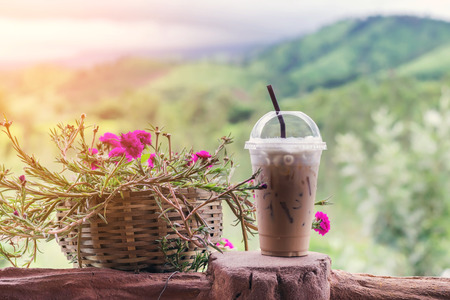 Closeup ice coffee in plastic cup with beautiful flower on  mountain background.の写真素材