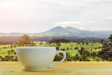 Close up of the white coffee mug on a wooden floor with the forest and mountain background.の写真素材