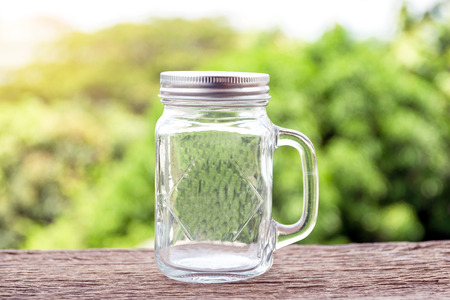 A glass jar with handle for drinks on wooden floor with green nature background.の写真素材