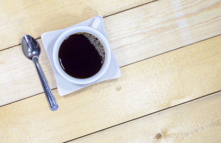 Top view of black coffee in a white ceramic coffee cup and stainless spoon on the wooden floor.の写真素材