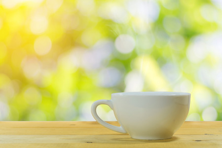 Close up of the white coffee mug on a wooden floor with a beautiful green nature background.の写真素材