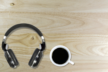 Top view of black coffee in a white ceramic coffee cup and the wireless headphone on a wooden floor.の写真素材