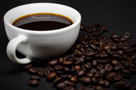 Closeup coffee beans and white ceramic coffee mug on the dark background.の写真素材