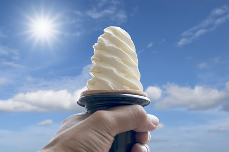Hand holding ice cream cone on the sky and sunlight background.の写真素材