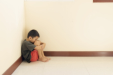 Blurred of the boy hugged her knees in tears in a corner of the room.の写真素材